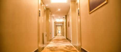 A hotel hallway with a carpeted floor, doors on both sides, and a ceiling light.