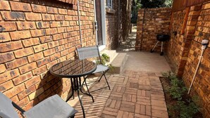 A brick patio with a round table and two chairs, surrounded by brick walls and a narrow pathway.