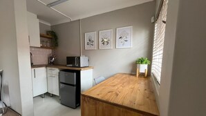 A compact kitchen with a wooden countertop, a refrigerator, a microwave, and a small potted plant.