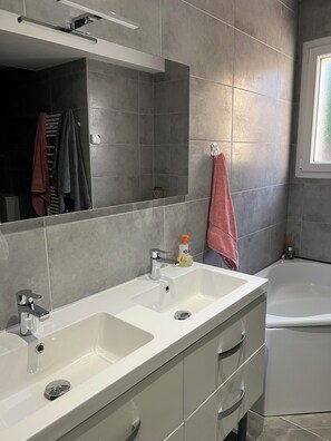 Un baño moderno con dos lavamanos, un espejo, un perchero para toallas y una bañera.