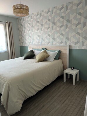 Una cama bien hecha con varias almohadas, una mesita de noche con una lámpara y una pared con diseño geométrico.