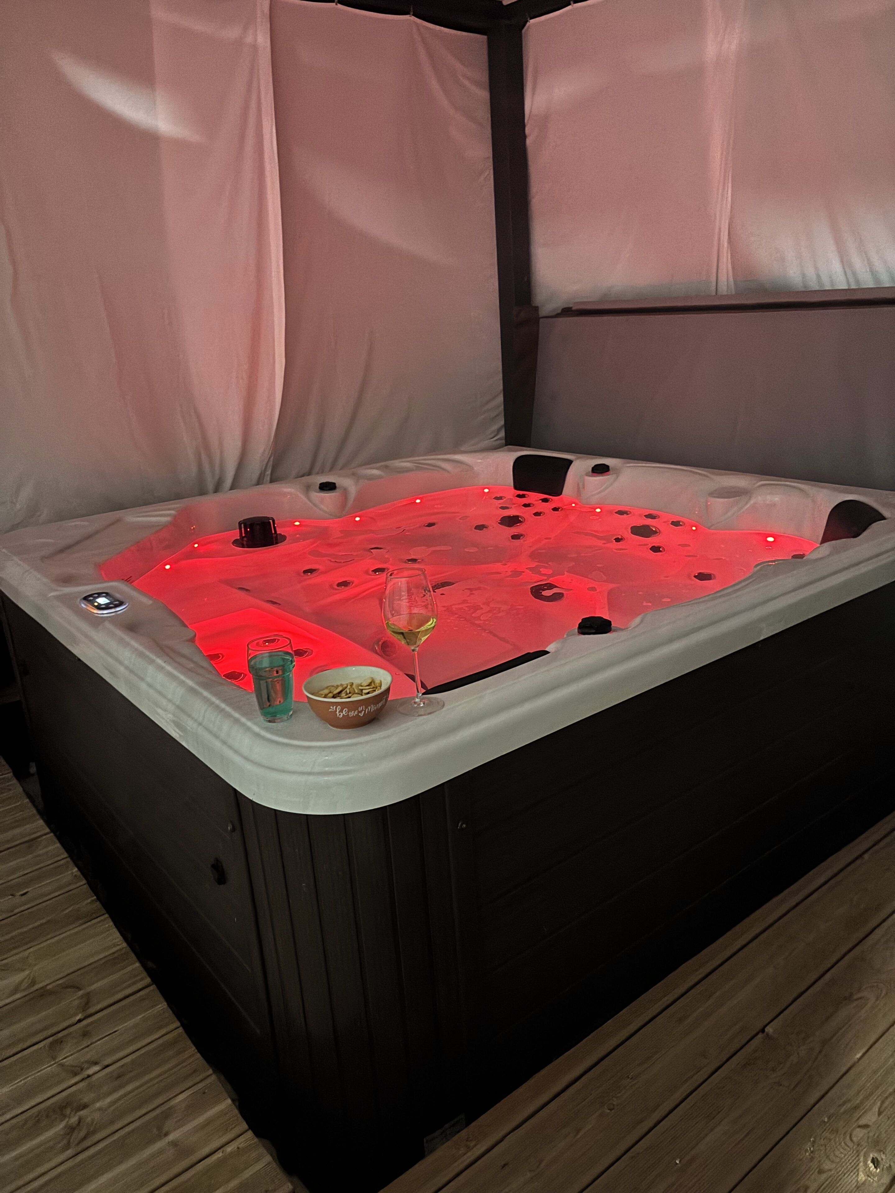 A hot tub with a glass of wine and a bowl of snacks on the side.