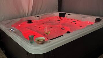 A hot tub with a glass of wine and a bowl of snacks on the side.