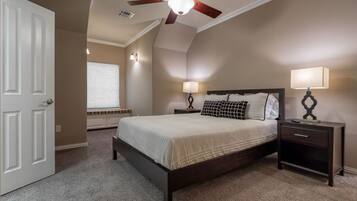 A bedroom with a bed, two bedside tables with lamps, a ceiling fan, and a window with blinds.