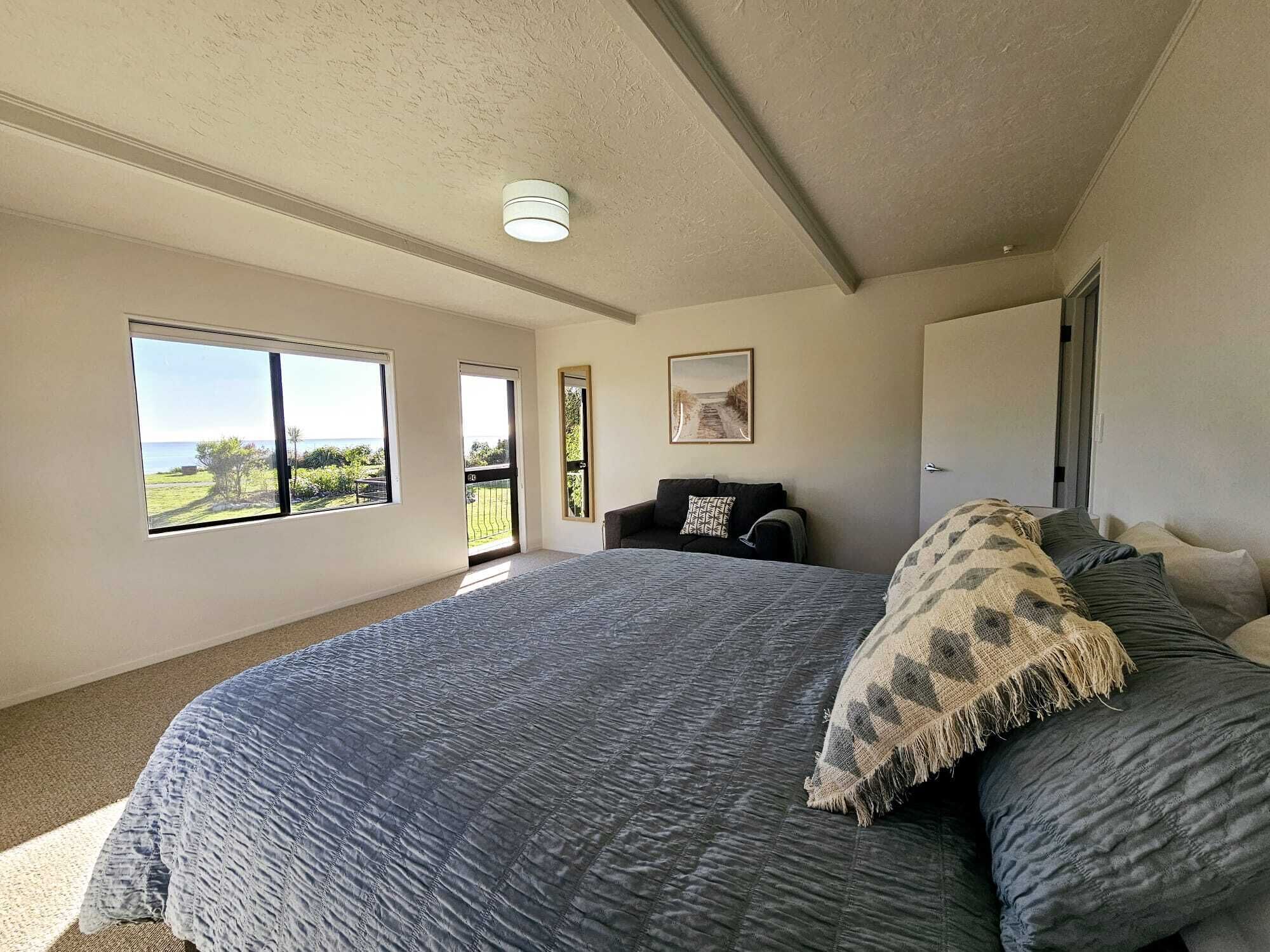 Un dormitorio con una cama grande, vistas al exterior a través de una ventana y una puerta que da a otra habitación.