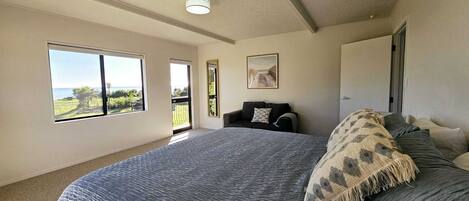 Un dormitorio con una cama grande, vistas al exterior a través de una ventana y una puerta que da a otra habitación.