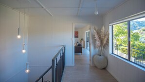 A hallway with pendant lights, a large window with a view, and a potted plant with pampas grass. - BEACH FRONT - Sunflower Beach House Pohara (Pōhara)