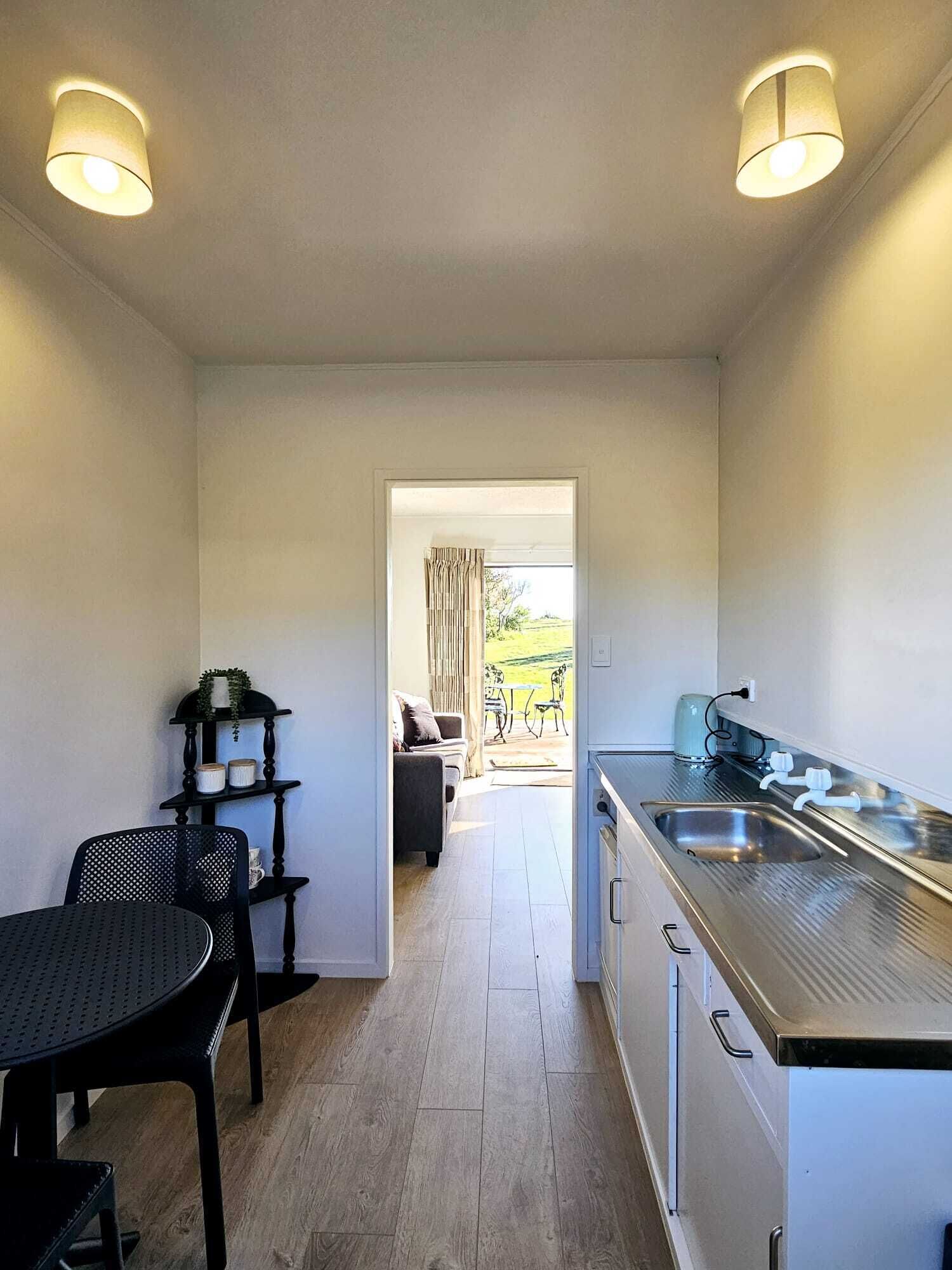 A compact kitchen with a central island, a dining area with a table and chairs, and a view of the outdoors through a doorway.