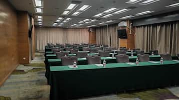 A conference room with rows of tables, chairs, and water bottles, equipped with a projector and curtains.