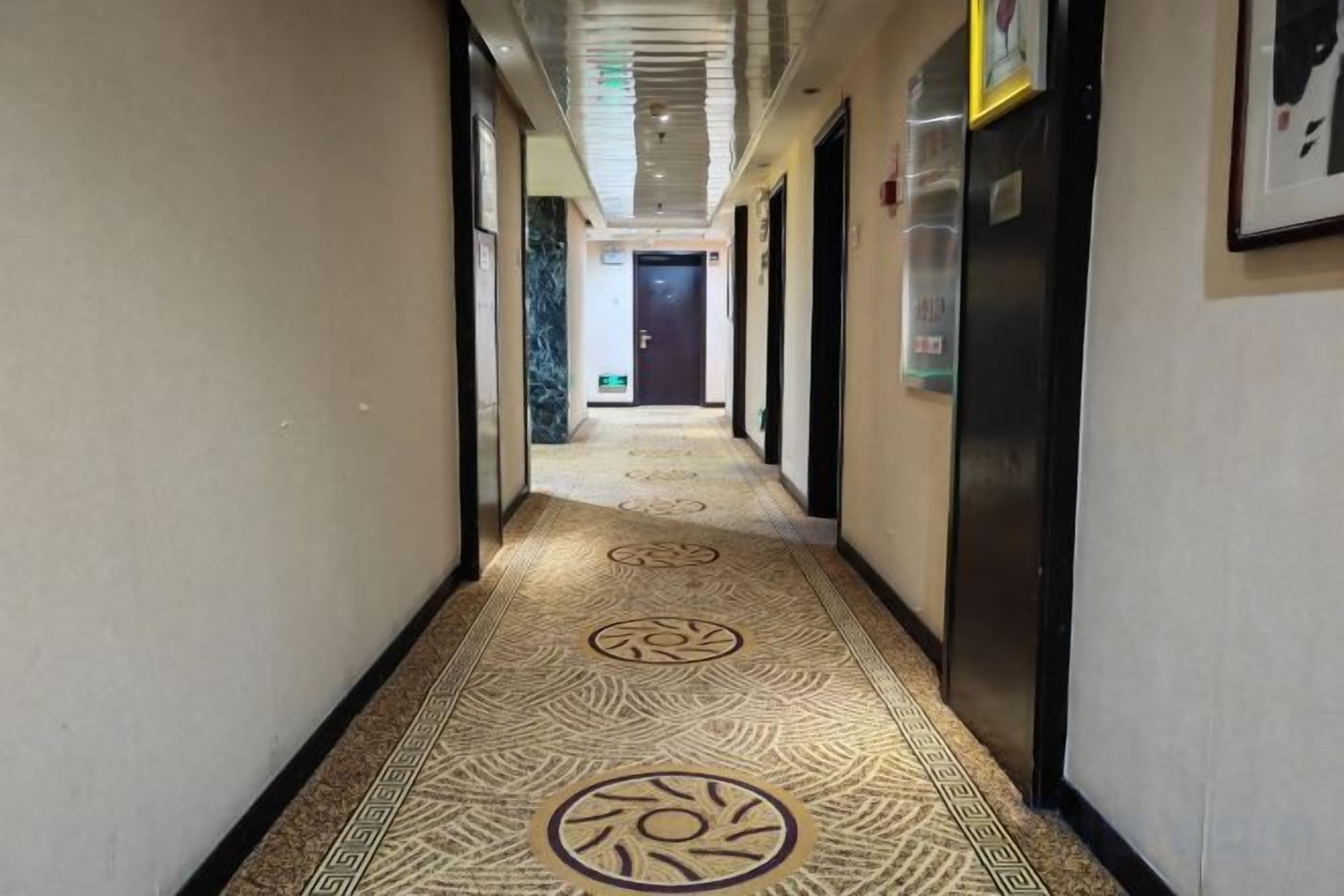 Un couloir d’hôtel avec un tapis à motifs, des portes et un réfrigérateur.
