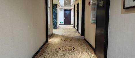 A hotel hallway with patterned carpet, doors, and a refrigerator.