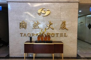 A hotel entrance with a marble wall, a reception desk, and a sign with the hotel's name in both Chinese and English. - Taoran Hotel (Beijing)