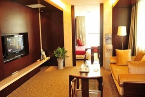 A hotel room with a TV, a sofa, a coffee table, a plant, and a bed. - Taoran Hotel (Beijing)