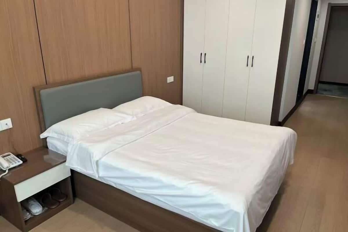 A single bed with a wooden headboard, a bedside table with a phone, and a wardrobe with two doors.