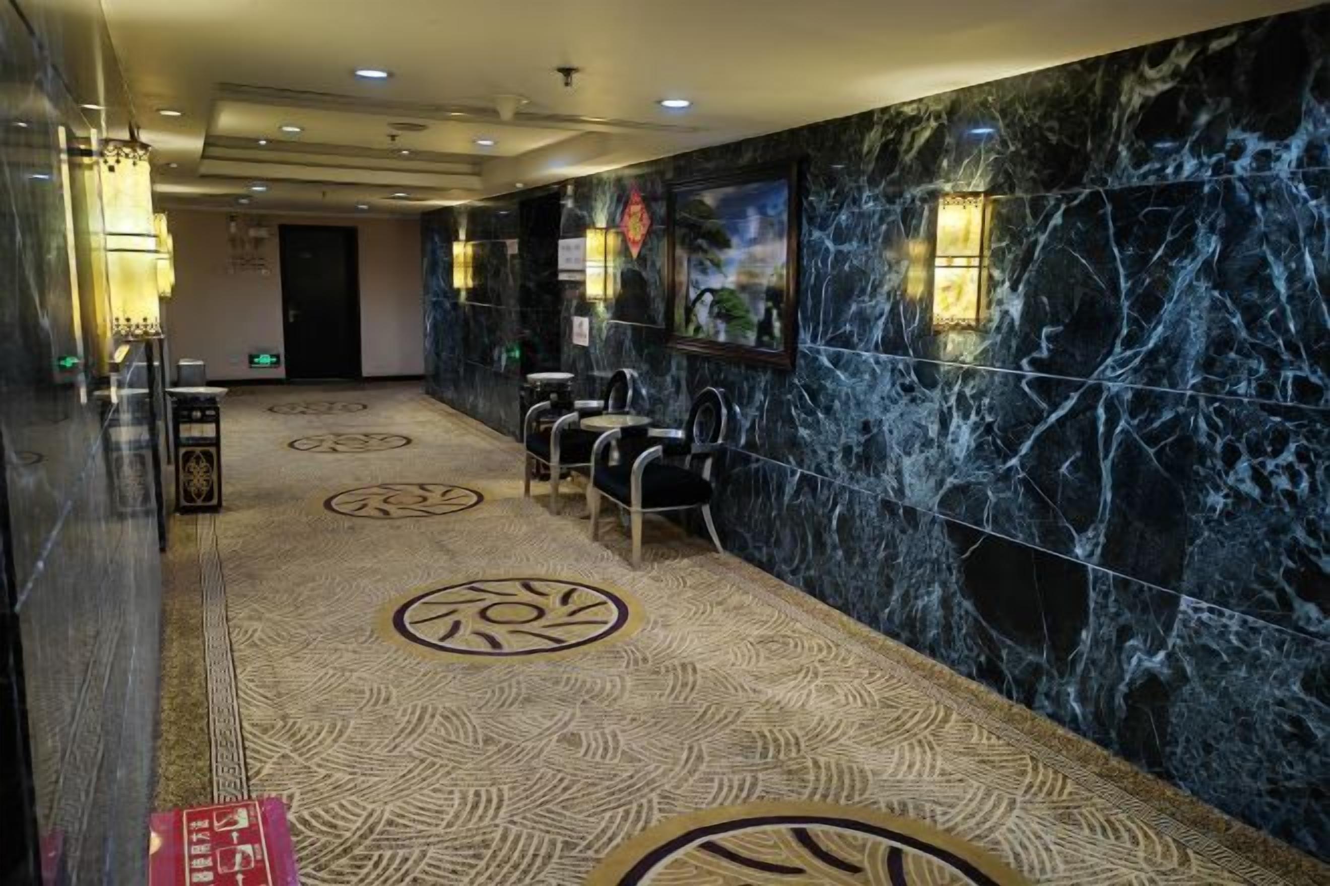 Um saguão de hotel com parede de mármore, carpete estampado e área de estar.