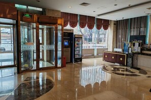 Un hall d’hôtel comprenant un comptoir d’accueil, un kiosque en libre-service et une entrée avec une porte en verre.