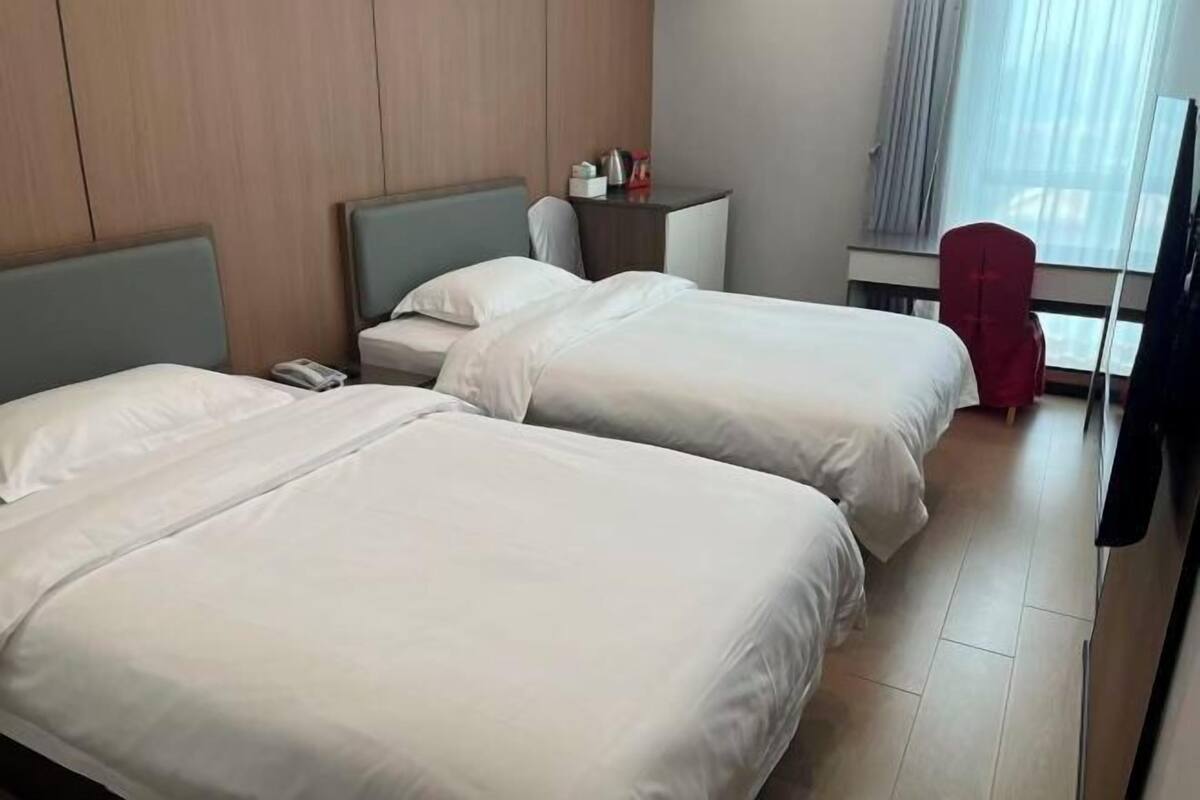 A hotel room with two beds, a small desk, a chair, and a window with curtains.