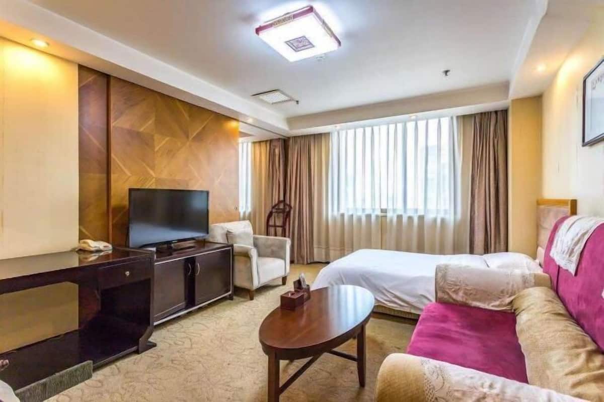 A hotel room with a bed, a TV, a desk, a chair, and a window with curtains.