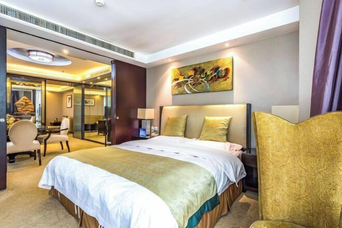 A hotel room with a large bed, a desk, a chair, and a mirror.
