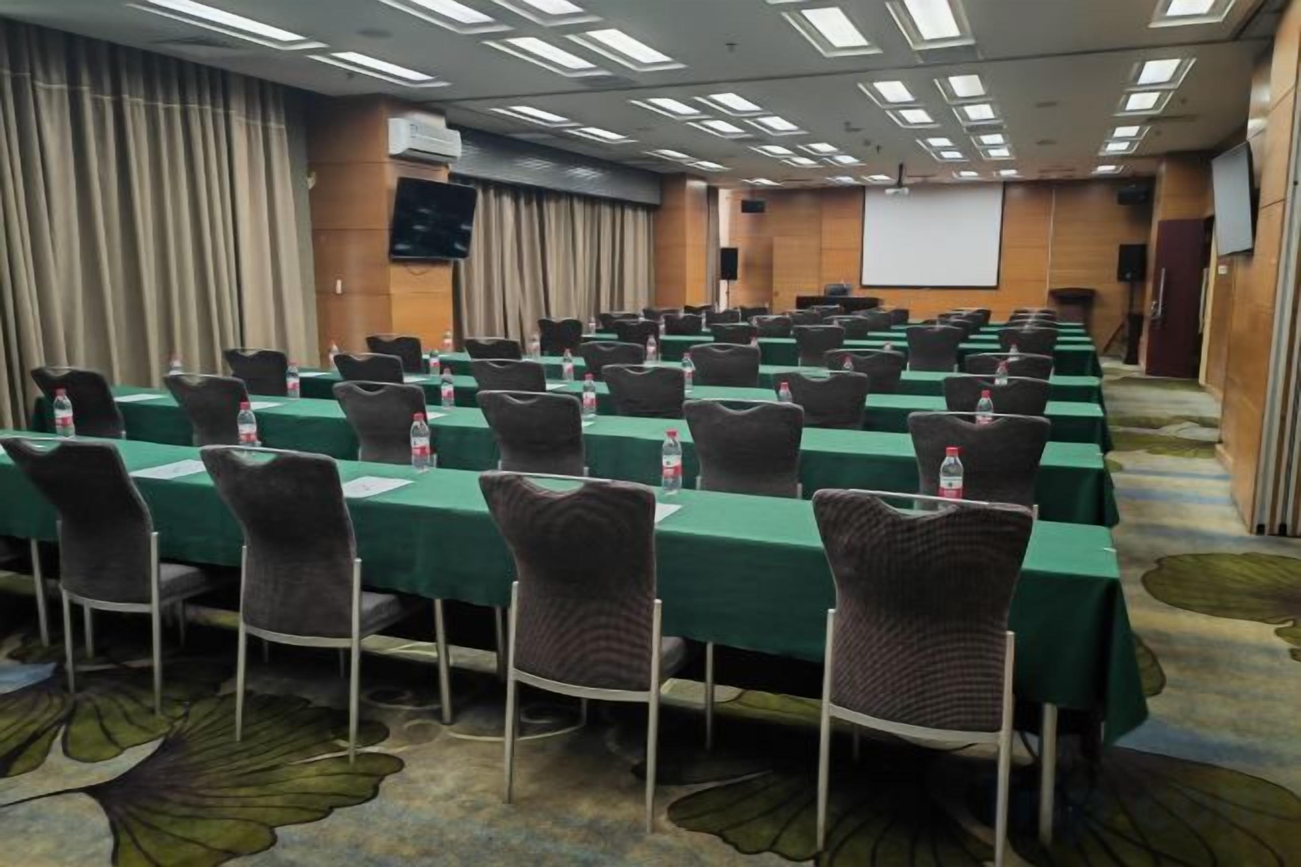 Une salle de conférence équipée de plusieurs tables et chaises, d’un écran de projection et d’un sol recouvert de moquette.