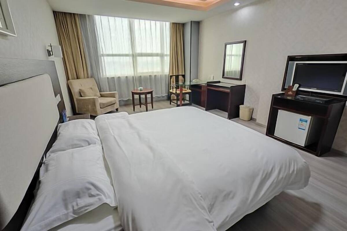 A hotel room with a large bed, a desk, a chair, a television, and a window with curtains.
