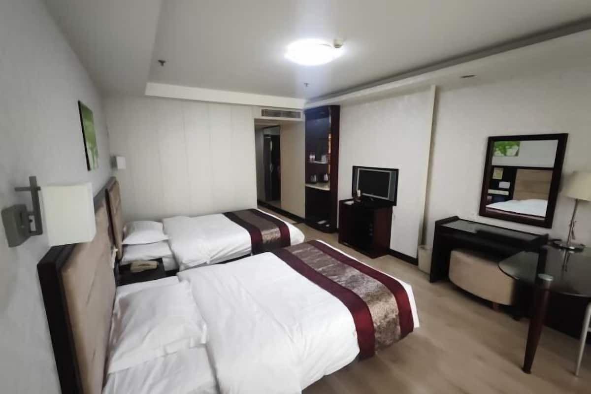 A hotel room with two beds, a desk, a chair, a TV, and a mirror.