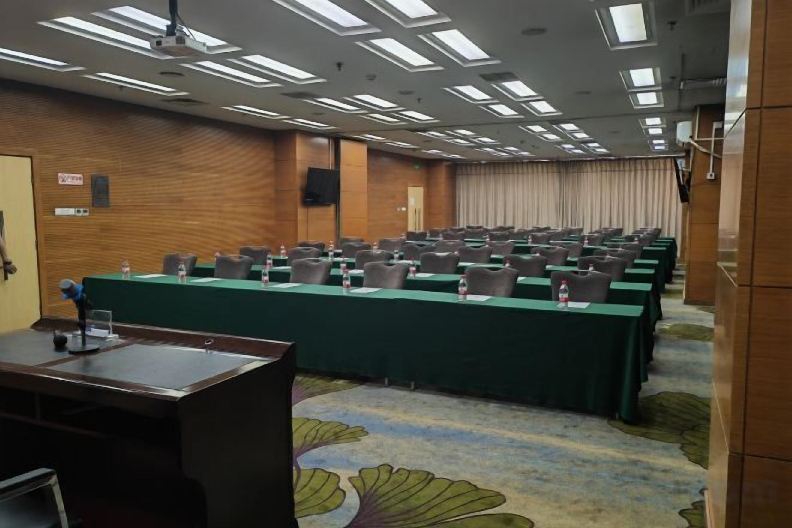 Un salón de conferencias con filas de mesas y sillas, un atril y suelo alfombrado.