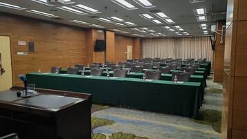 A conference room with rows of tables and chairs, a podium, and a carpeted floor.