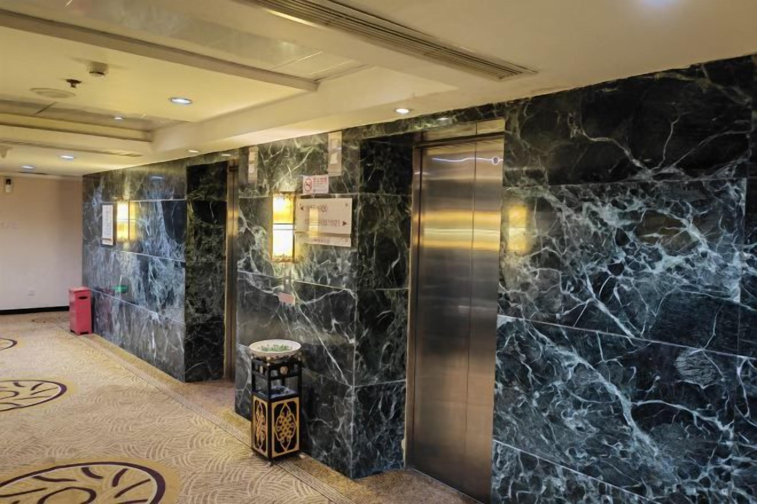 Um hall de hotel com paredes de mármore, um elevador e um tapete estampado.