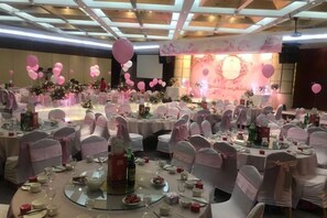 A banquet hall with round tables, chairs, and a stage with a floral backdrop. - Taoran Hotel (Beijing)