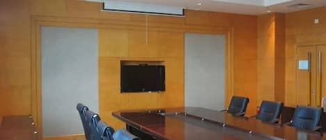A conference room with a long table, several chairs, a flat-screen TV, and a wooden panel wall.