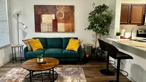 A modern living room with a green sofa, yellow cushions, a round coffee table, and a large abstract painting on the wall.
