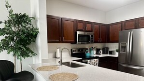 A modern kitchen with dark wooden cabinets, stainless steel appliances, a granite countertop, and a black chair.