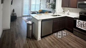 A modern kitchen with dark wood flooring, white cabinetry, and stainless steel appliances.