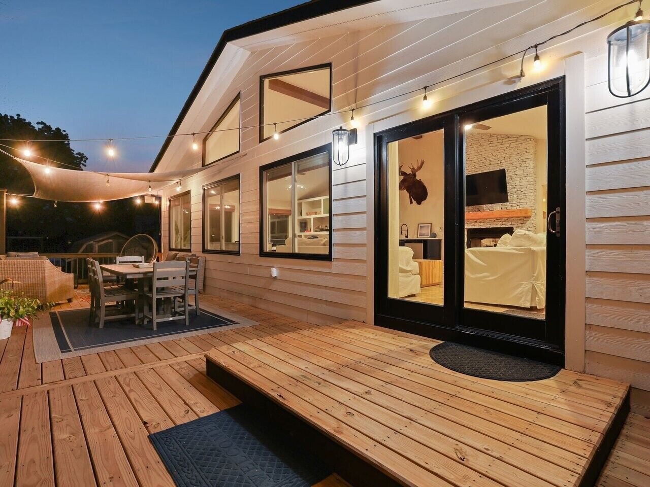 A wooden deck with a dining area and a sliding glass door leading to a room with a bed and a mounted animal head decoration.