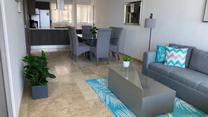 A modern living room with a grey sofa, a coffee table, and a dining area with chairs and a table. - BEAUTIFUL BEACHFRONT APARTMENT, ACAPULCO COASTLINE ARMANDOS LE CLUB (Acapulco de Juárez)