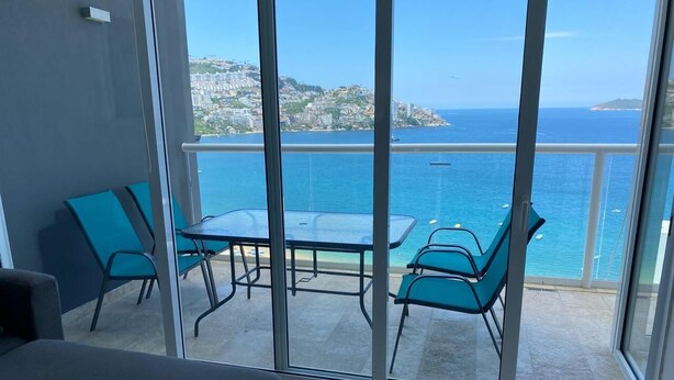 A balcony with a glass door, a small table, and two chairs. - BEAUTIFUL BEACHFRONT APARTMENT, ACAPULCO COASTLINE ARMANDOS LE CLUB (Acapulco de Juárez)