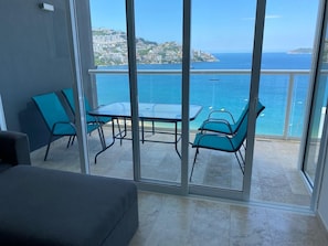 Enjoy the breathtaking sea views from this balcony with a glass door leading to a seating area with a table and chairs.