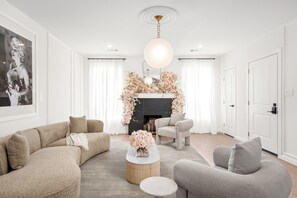 Un salon moderne avec un canapé, un fauteuil et une table basse. On y trouve une cheminée décorée de motifs floraux et un luminaire suspendu.