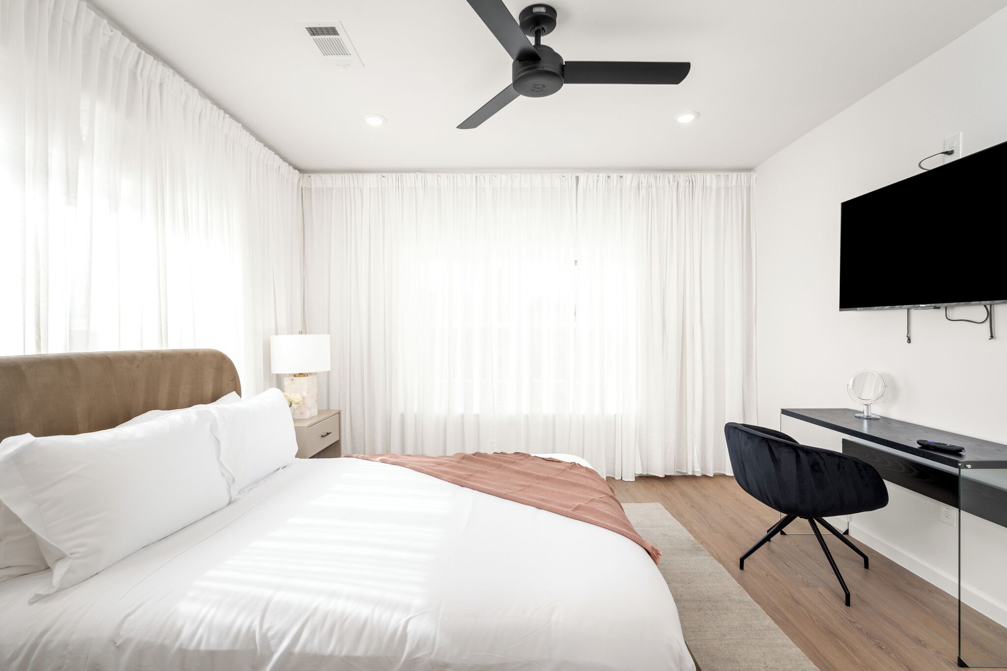 Una habitación de hotel moderna con una cama, un escritorio, una silla, un ventilador de techo y un televisor.