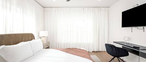 Una habitación de hotel moderna con una cama, un escritorio, una silla, un ventilador de techo y un televisor.