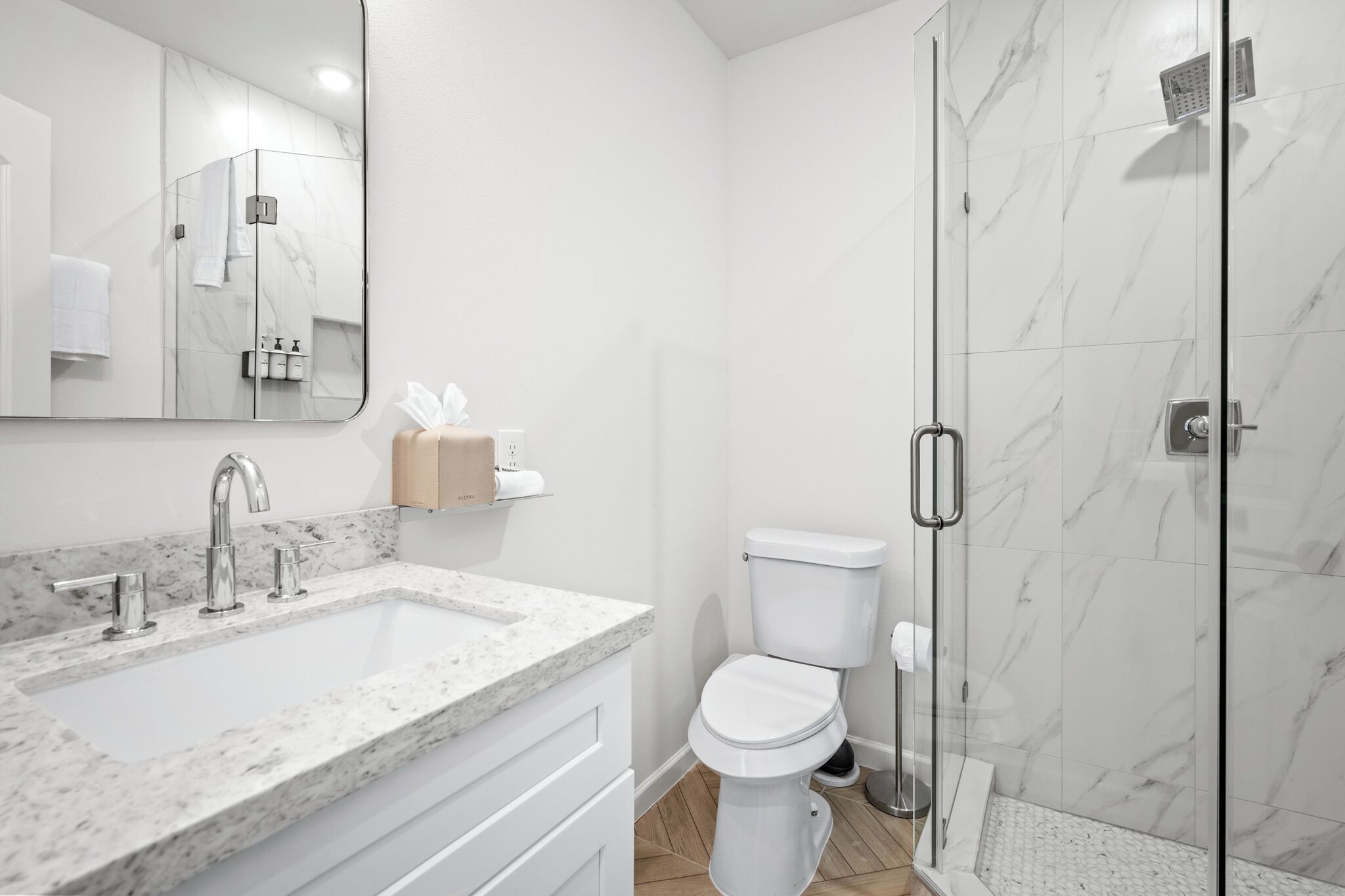 A modern bathroom with a marble sink, a toilet, and a glass-enclosed shower.
