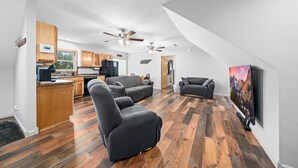 A spacious living area with a kitchen, two gray sofas, a flat-screen TV, and a wooden floor. - Backwoods Bungalow (Crossville)