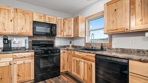 A kitchen with wooden cabinets, a black stove, a microwave, a sink, and a dishwasher. - Backwoods Bungalow (Crossville)