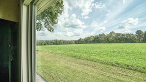 A view from a window overlooking a grassy field with trees in the distance. - Backwoods Bungalow (Crossville)