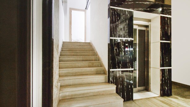 A staircase with wooden steps leading to a landing, a glass door, and a wall with a marble-like pattern. - Classic Devi Residency (Hyderabad)