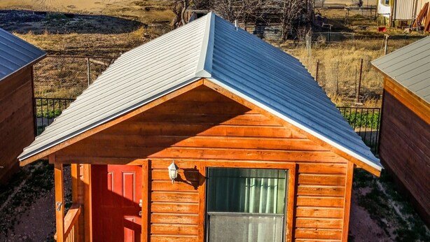 A small wooden cabin with a red door, a window with a curtain, and a metal roof. - Cozy cabin with AC and WiFi in peaceful Sterling City.  Your small town adventure awaits! (Sterling City)