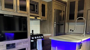 Une cuisine moderne avec des meubles en bois, des appareils en acier inoxydable et un îlot central illuminé de lumière bleue.