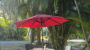 Un espace extérieur aménagé avec une table et des chaises, un parasol rouge et de la verdure tout autour.