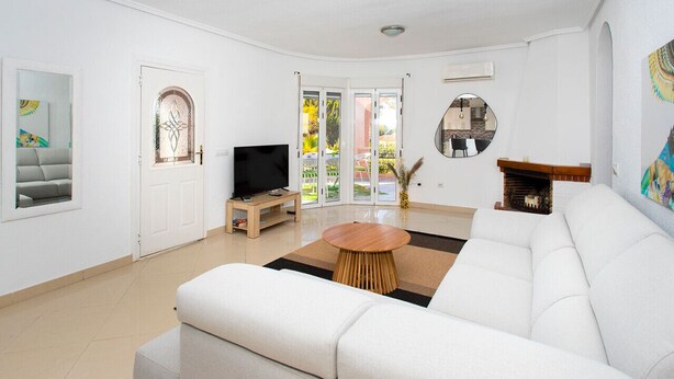 Una sala de estar moderna con un sofá blanco, una mesa de centro de madera, un televisor y una chimenea.